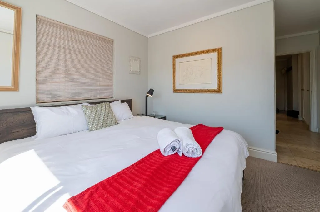 Bright bedroom with queen bed, white linens, red throw, and framed artwork