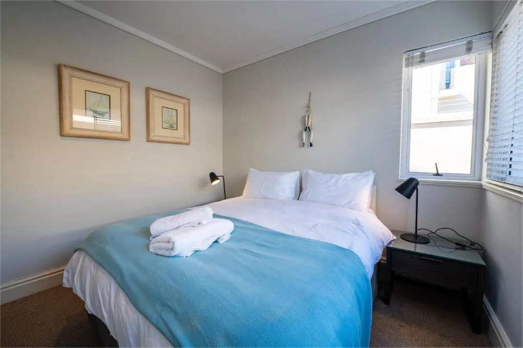 Bright bedroom with queen bed, white pillows, blue throw, and framed wall art