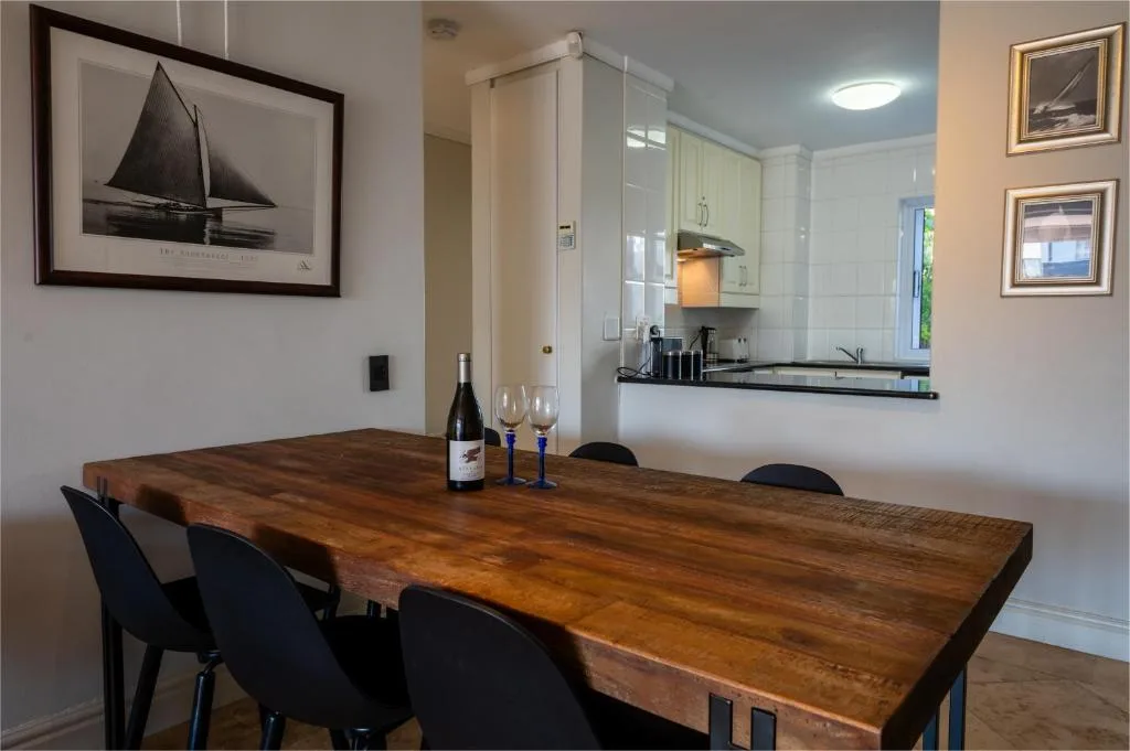 Wooden dining table with black chairs, wine bottle, and glasses displayed