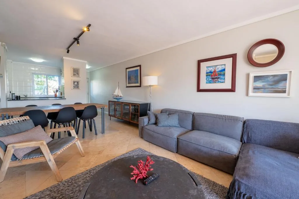Open-plan lounge with gray sectional sofa, framed coastal artwork, and dining area beyond