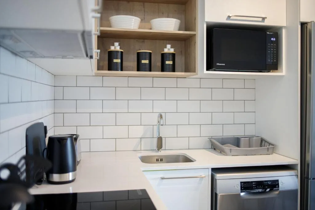 Modern kitchen with white subway tile, sink, microwave, and open shelving with storage