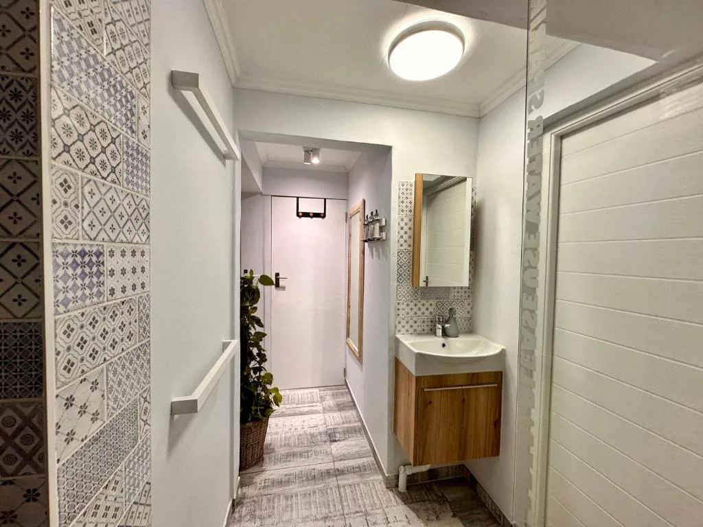 Modern bathroom with patterned tile walls, wooden vanity, and round ceiling light