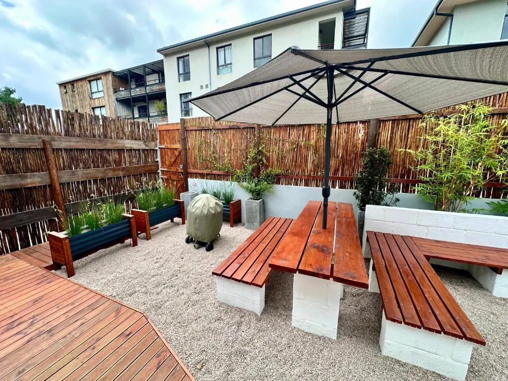 Outdoor patio with wooden picnic tables, umbrella, and garden seating area