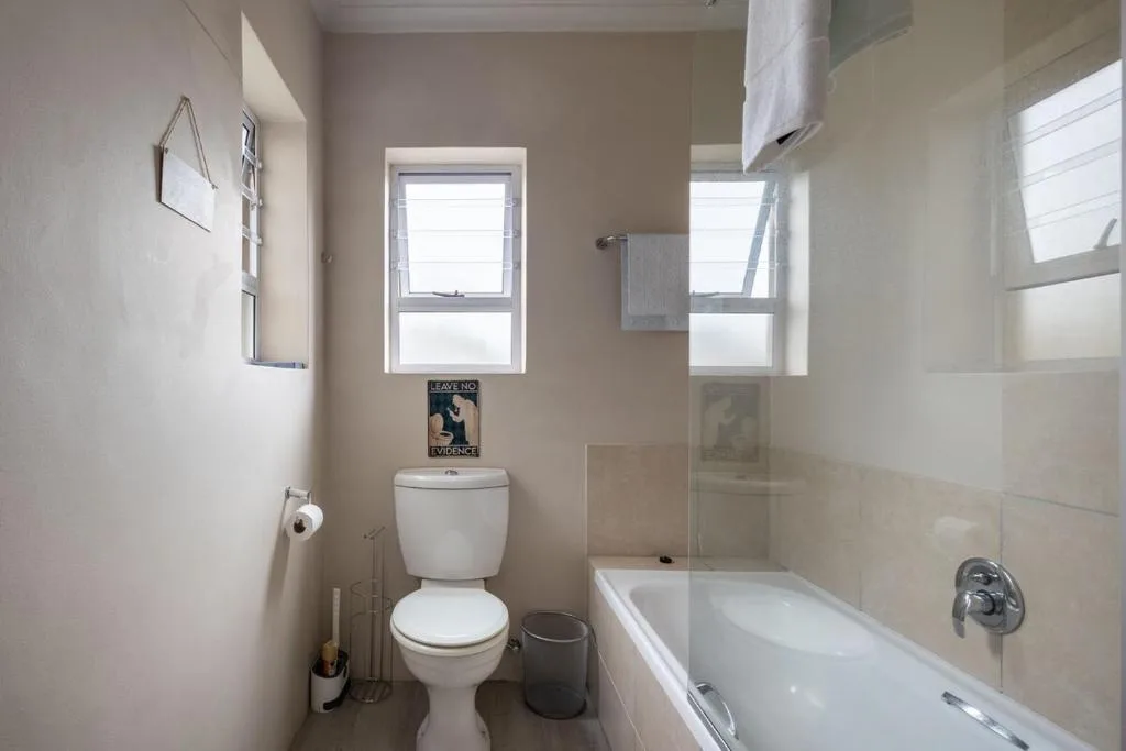 Clean bathroom with toilet, bathtub, shower area, and bright windows
