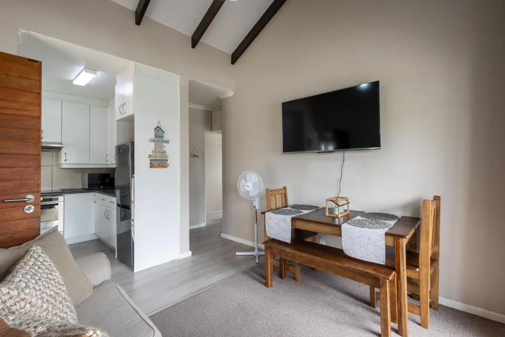 Open-plan lounge with dining table, wall-mounted TV, and kitchen access