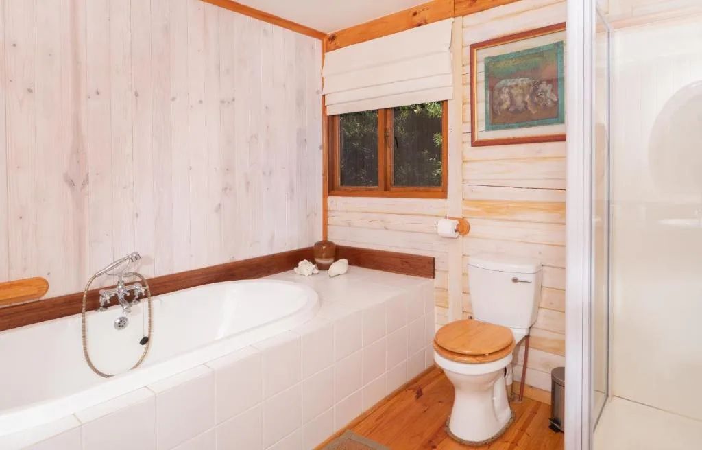 Rustic bathroom with wooden beams, white tile bathtub, and toilet