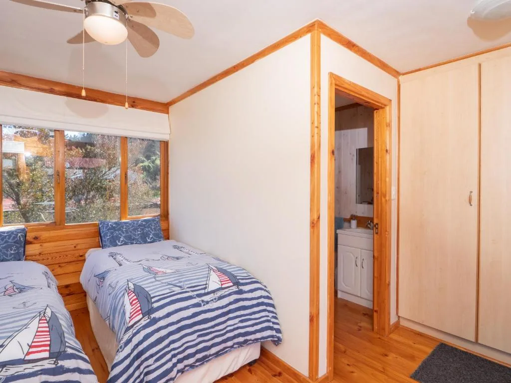 Bright bedroom with twin beds, wooden beams, and large windows overlooking garden
