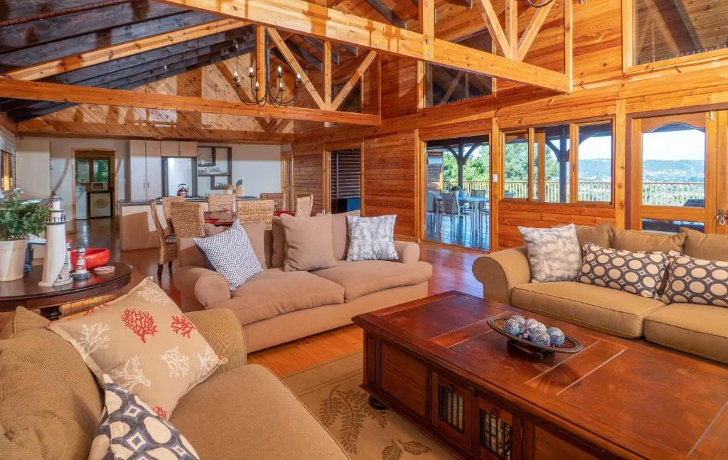 Spacious lounge with multiple sofas, wooden beams, and panoramic windows overlooking landscape views
