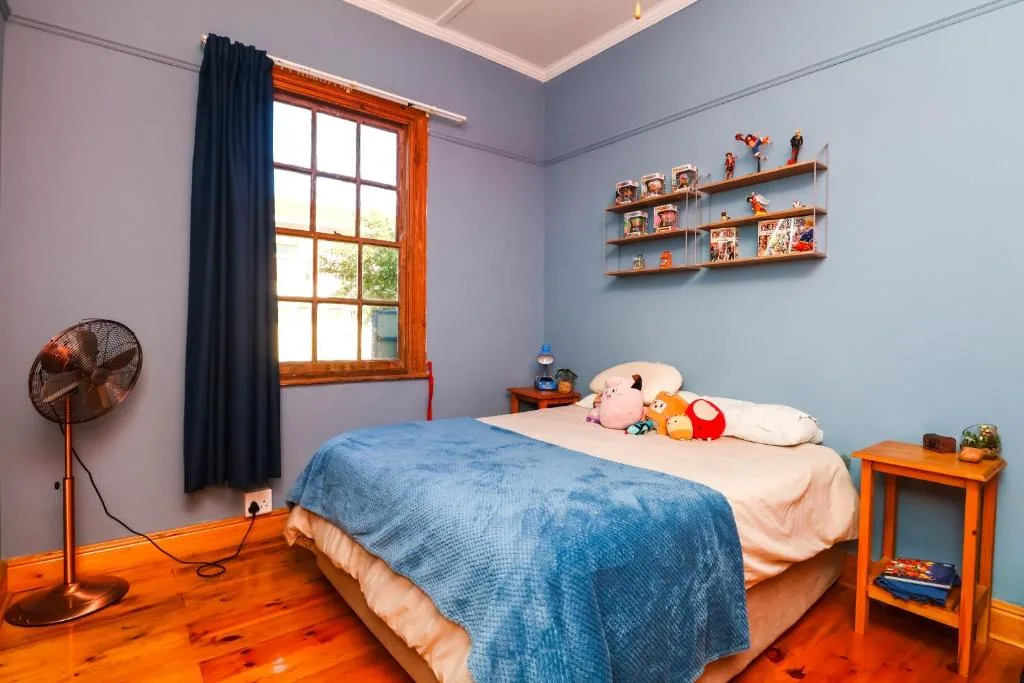 Bright bedroom with blue bedding, wooden frame window, and orange nightstand