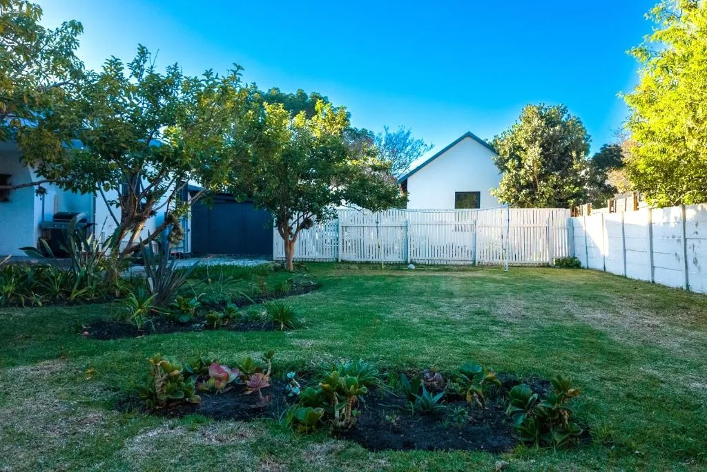 White cottage with fenced garden and mature trees under blue sky