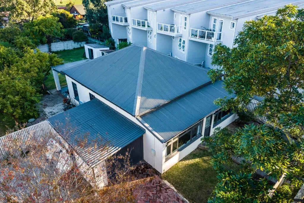Aerial view of modern white house with blue corrugated metal roofs and manicured gardens