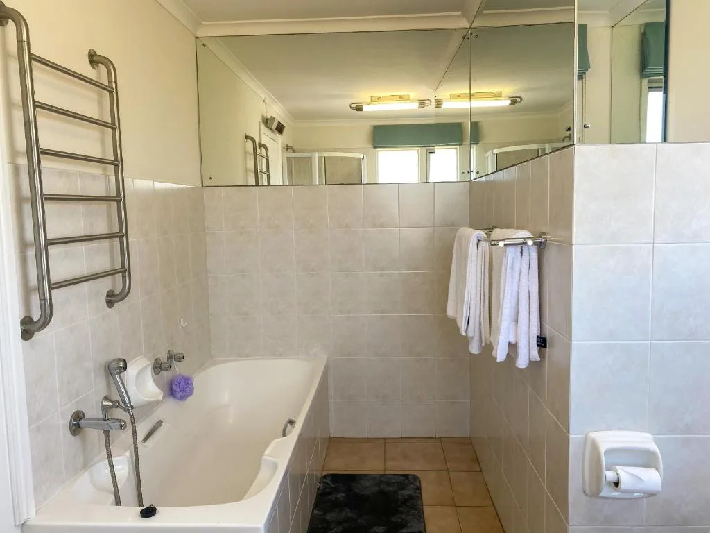 Spacious bathroom with bathtub, heated towel rack, and vanity mirror