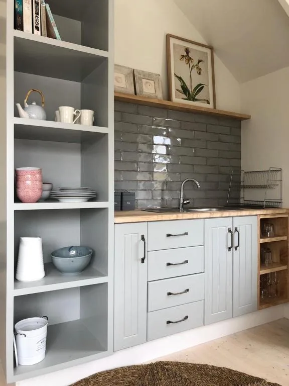 Modern kitchenette with white cabinetry, dark tile backsplash, open shelving