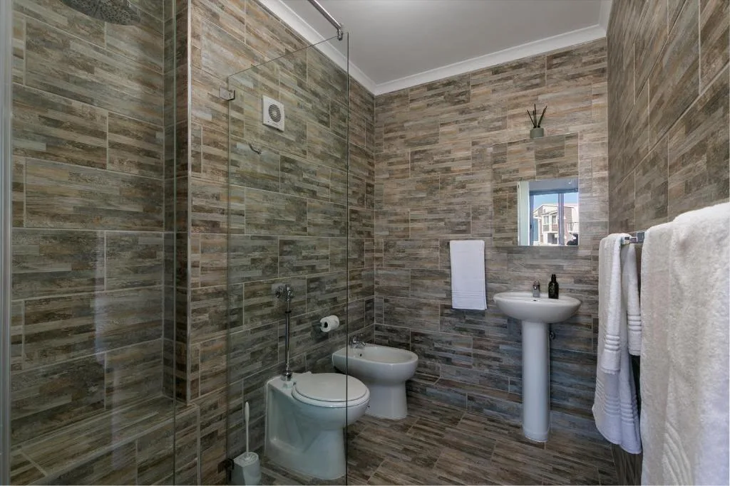 Modern bathroom with wood-grain tiled walls, walk-in shower, and pedestal sink