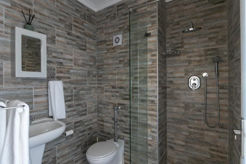 Modern bathroom with wood-look tile walls, glass shower enclosure, toilet, and vanity mirror