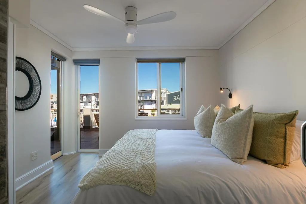 Bright bedroom with queen bed, decorative pillows, ceiling fan, and town views