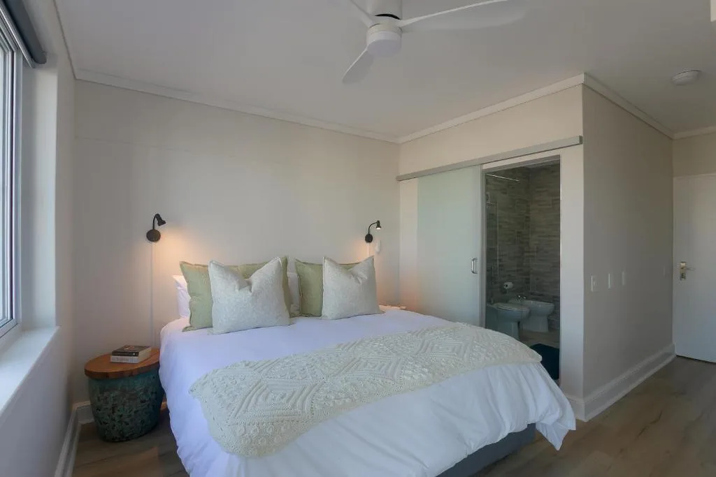 Modern bedroom with queen bed, green cushions, wall sconces, ensuite bathroom visible