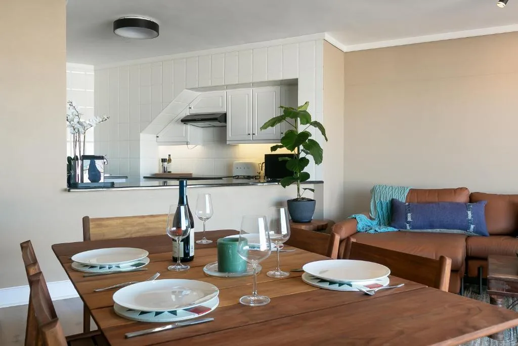 Wooden dining table set for three with kitchen and lounge visible beyond