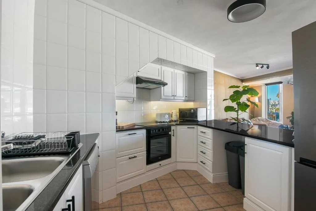 Modern white kitchen with black countertops, stainless steel appliances, and tile flooring