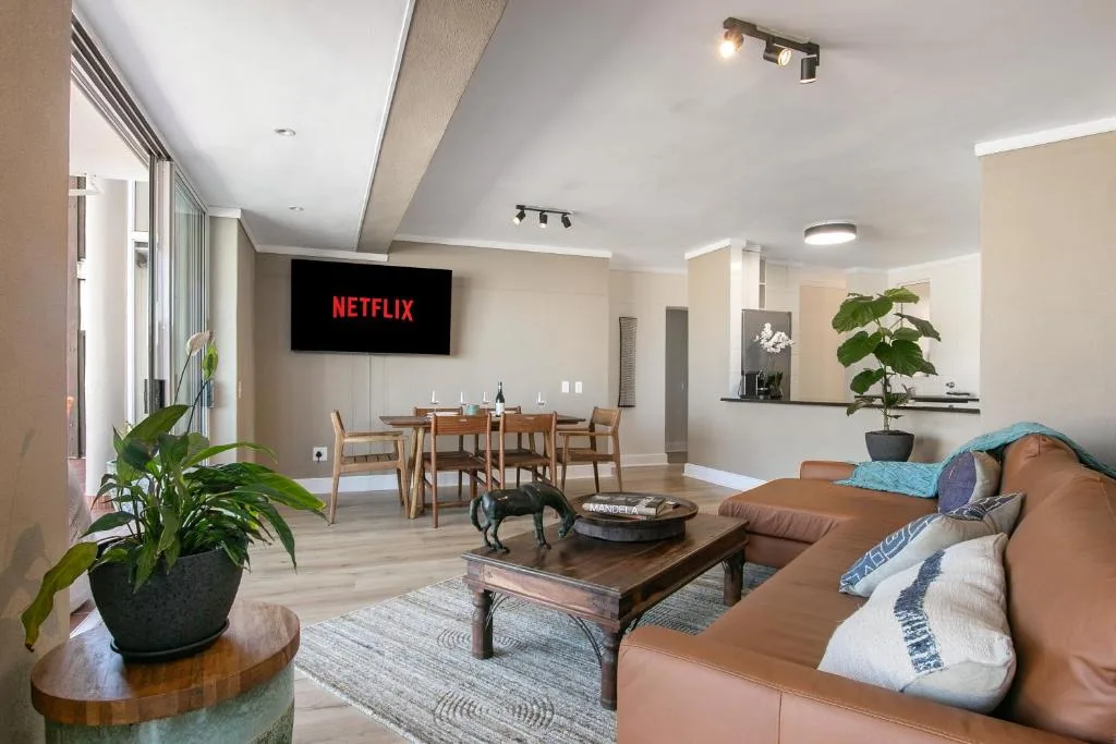 Open-plan lounge with tan leather sofa, TV, and dining area visible beyond