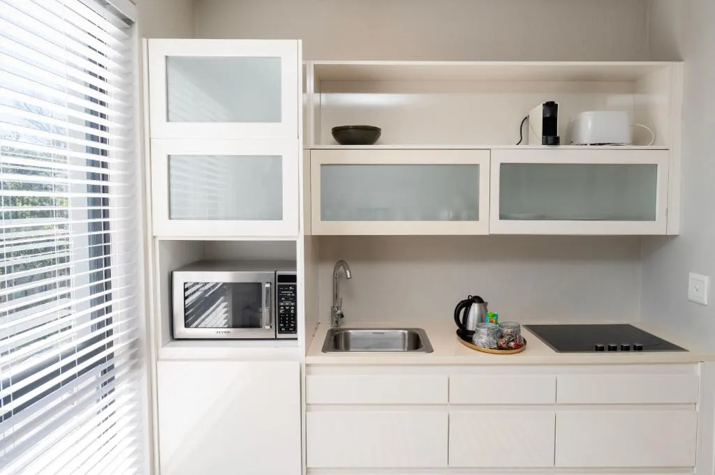 Modern white kitchen with microwave, sink, cooktop, and open shelving