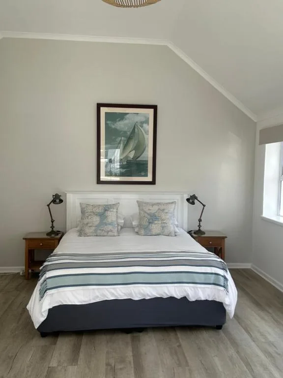 Bright bedroom with neatly made bed, sailboat artwork, and wooden nightstands