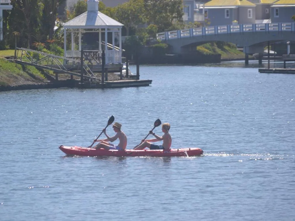 Kayakers paddling on calm lagoon water with white gazebo and bridge visible