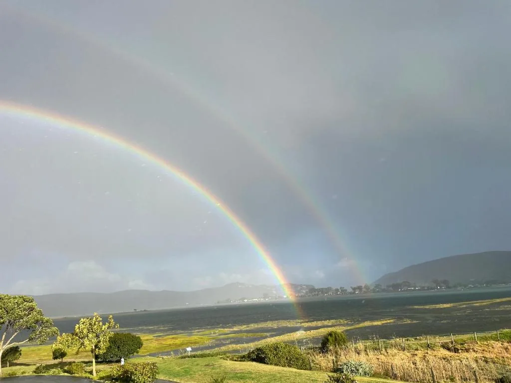 Rainbow stretching over Knysna Lagoon with surrounding mountains and lush green landscape