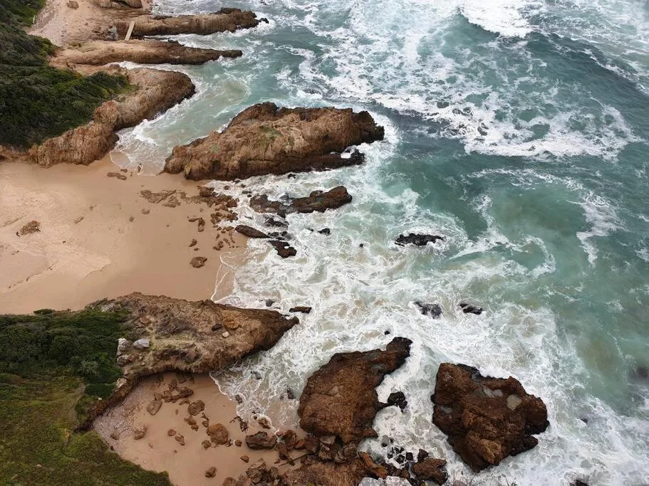 Aerial view of rocky coastline with crashing waves and sandy beach