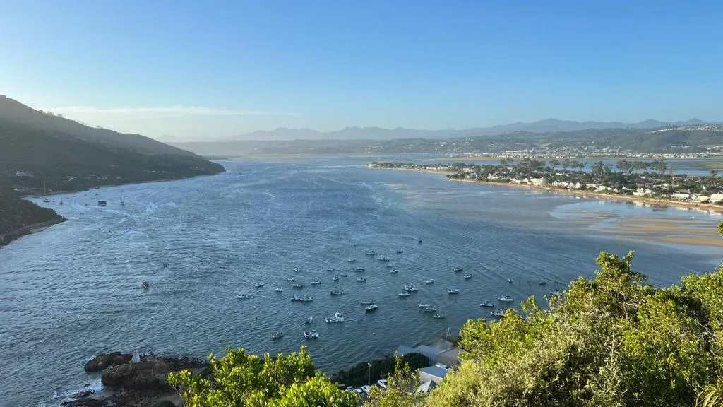 Expansive coastal bay view with moored boats, sandy beaches and mountains