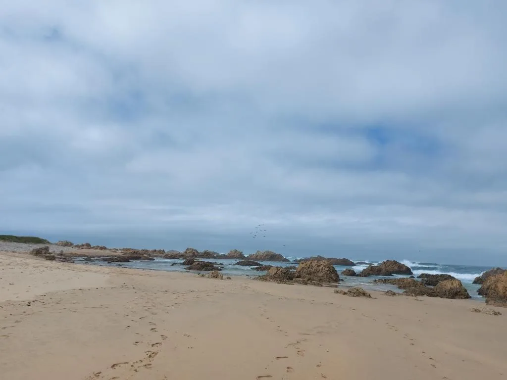 Scenic sandy beach with rocky outcrops and ocean waves under cloudy sky