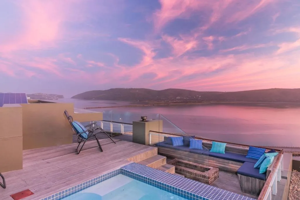Sunset-lit rooftop deck with pool, loungers, and lagoon views