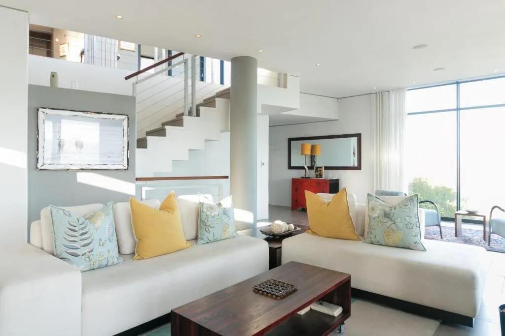 Bright open-plan lounge with cream sofas, yellow pillows, and staircase
