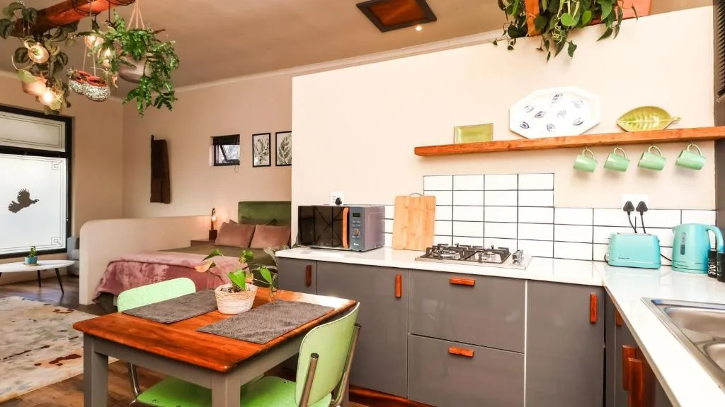 Modern kitchen with gas cooktop, turquoise kettle, wooden shelving, and dining table