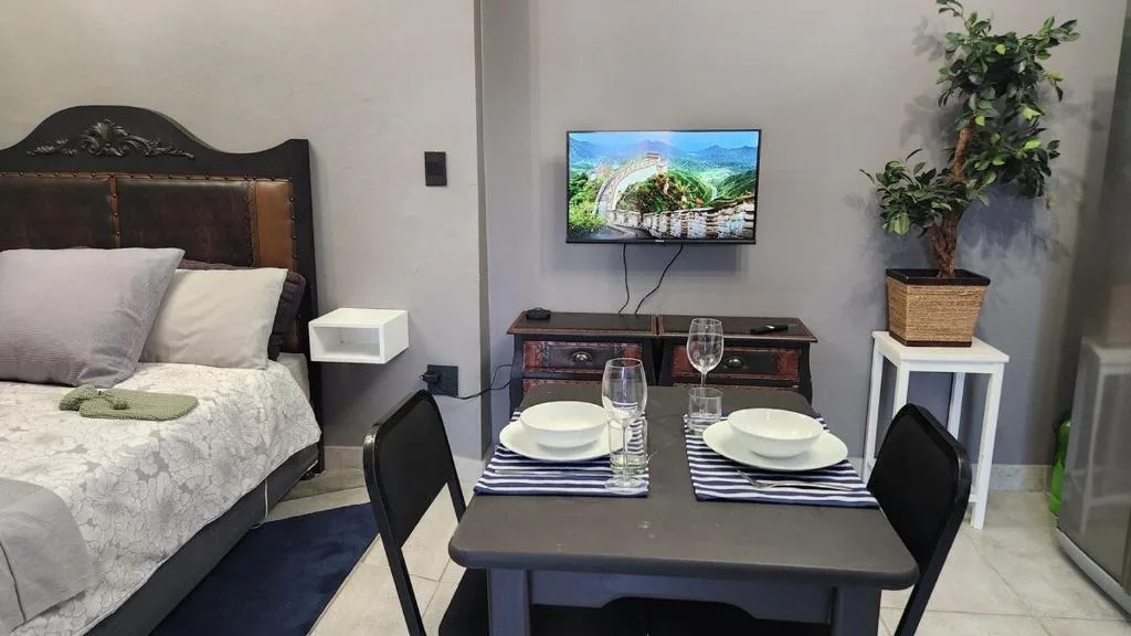 Studio apartment interior showing bed, dining table, and entertainment setup