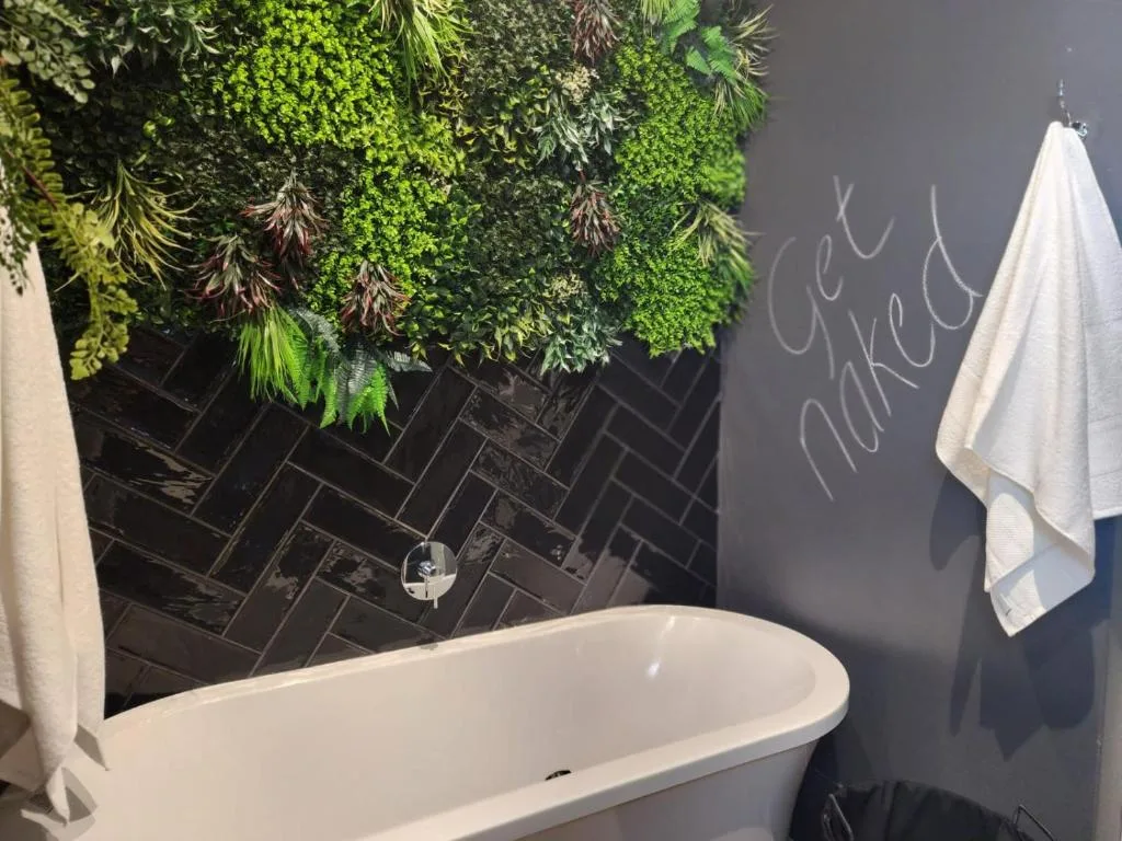 Modern bathroom with freestanding tub, black herringbone tiles, and green plant wall