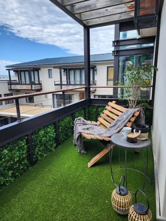 Modern balcony with wooden lounger, artificial grass, and mountain views