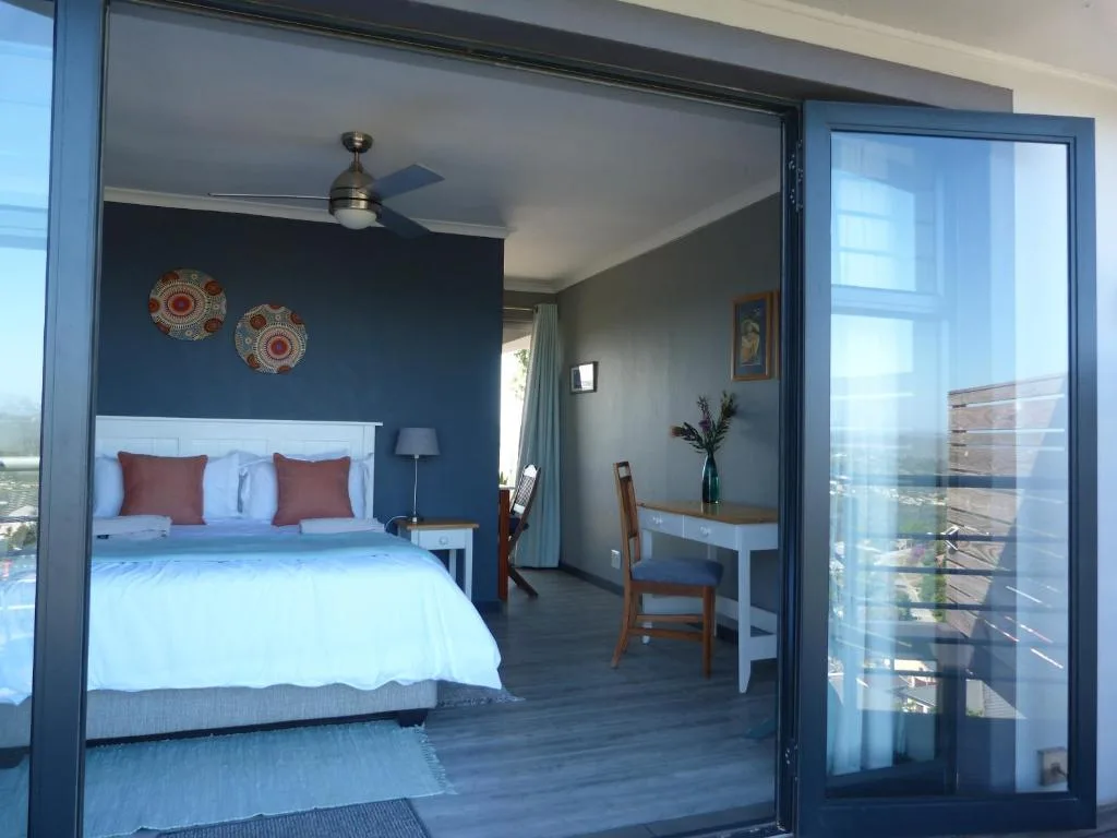 Modern bedroom with queen bed, navy accent wall, and ocean view through glass doors