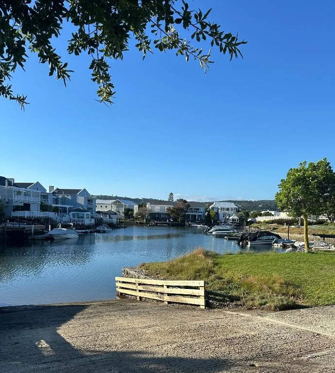 Waterfront lagoon view with boats, houses, and green hills under clear sky