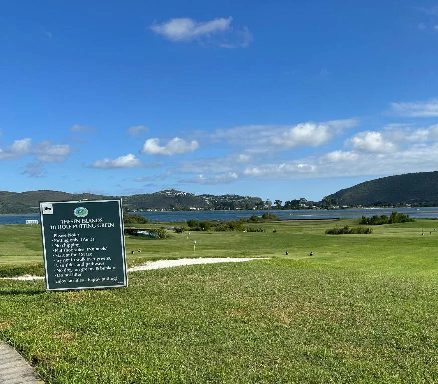 Scenic lagoon view with lush green fairway and distant mountains under blue sky