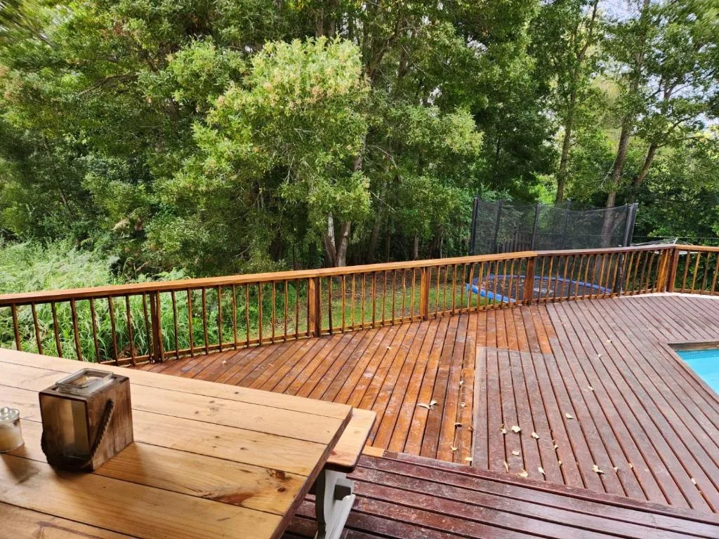 Wooden deck with metal railings overlooking lush garden and pool