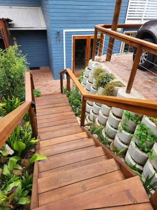 Wooden boardwalk leading to blue cottage with potted plants and railings