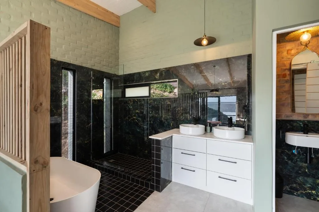 Modern bathroom with dual vanity sinks, black tile shower, and lagoon views