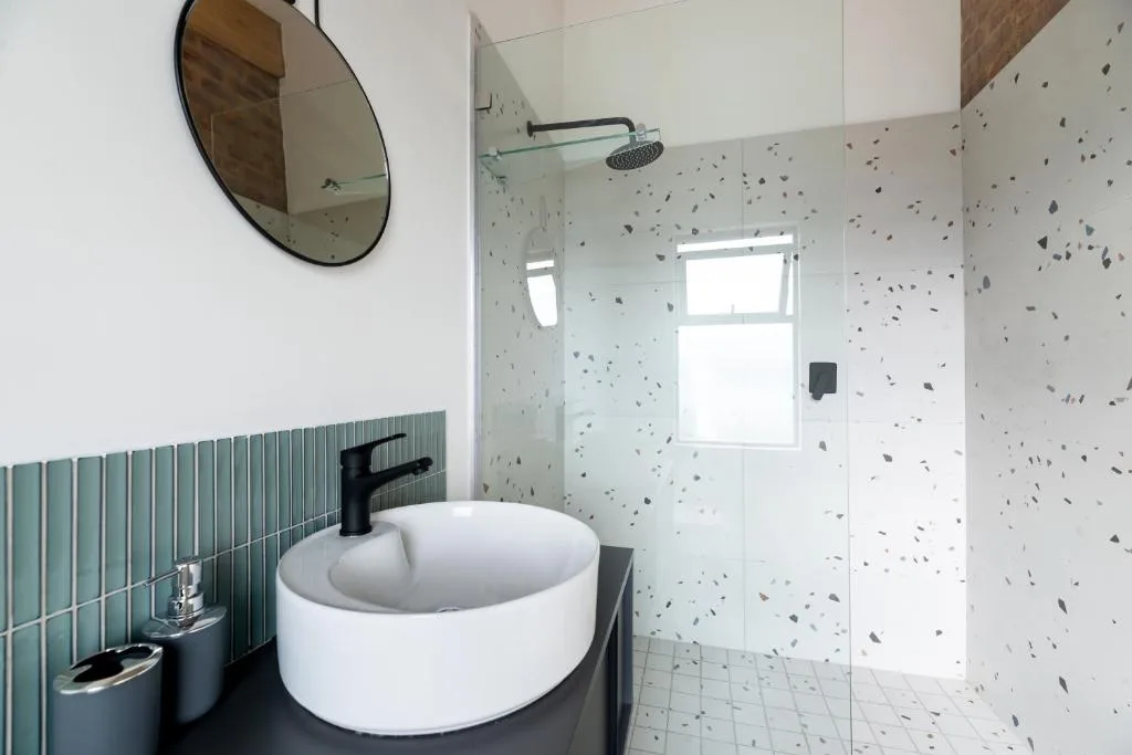 Modern bathroom with round white basin sink and rainfall shower enclosed by terrazzo tiles