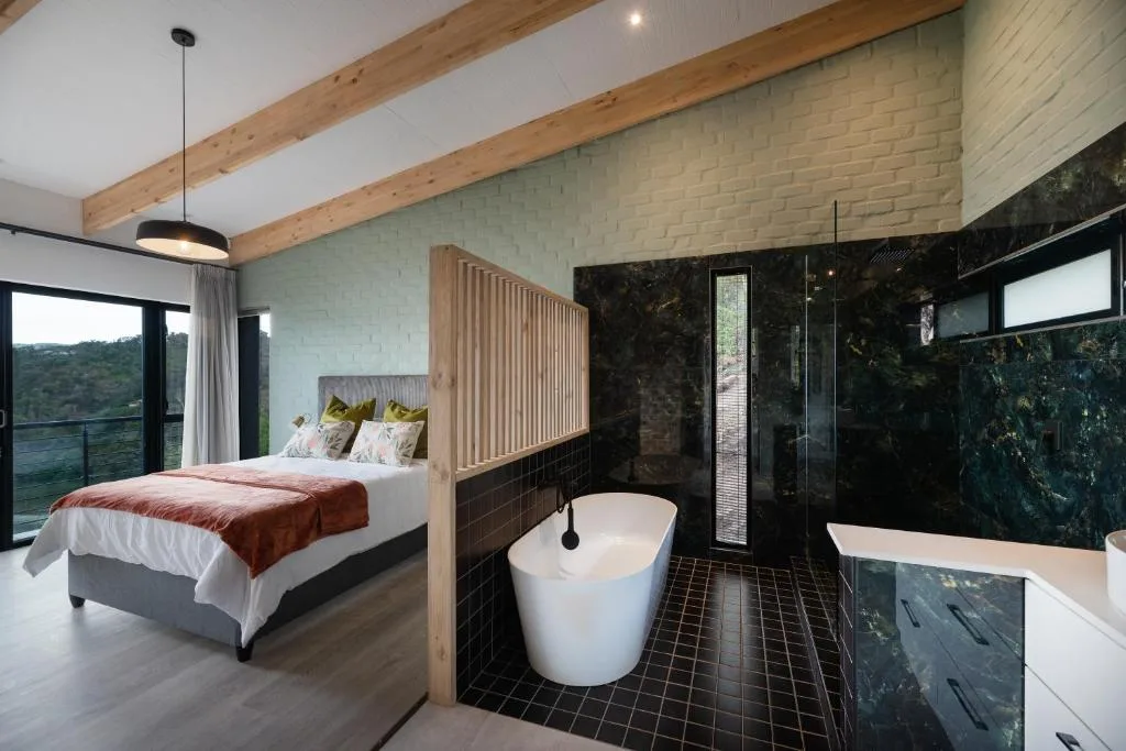 Modern bedroom with bed, en-suite bathroom featuring freestanding tub and view