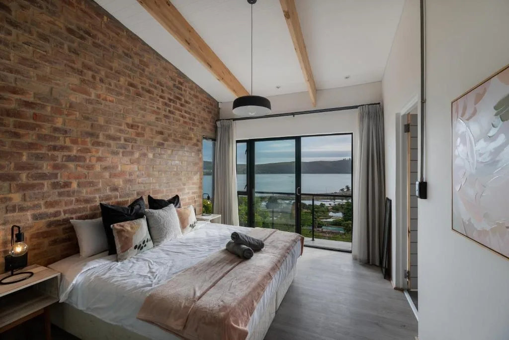 Modern bedroom with exposed brick wall and panoramic lagoon views through large windows