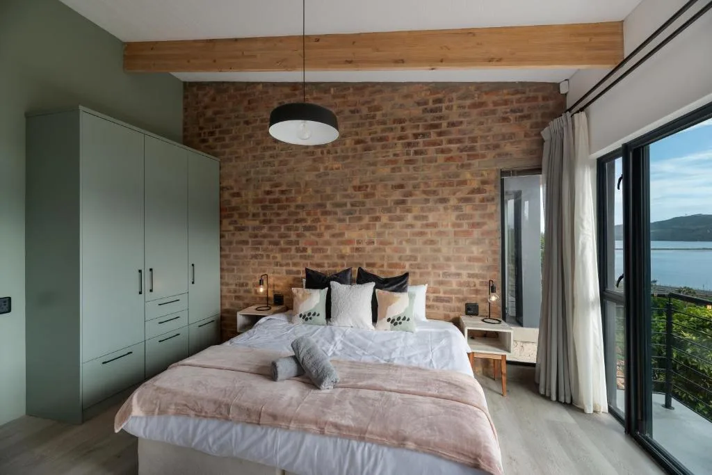 Modern bedroom with exposed brick wall, queen bed, and lagoon views through glass doors
