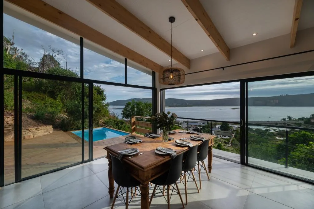 Dining table with lagoon views through floor-to-ceiling windows and pool beyond