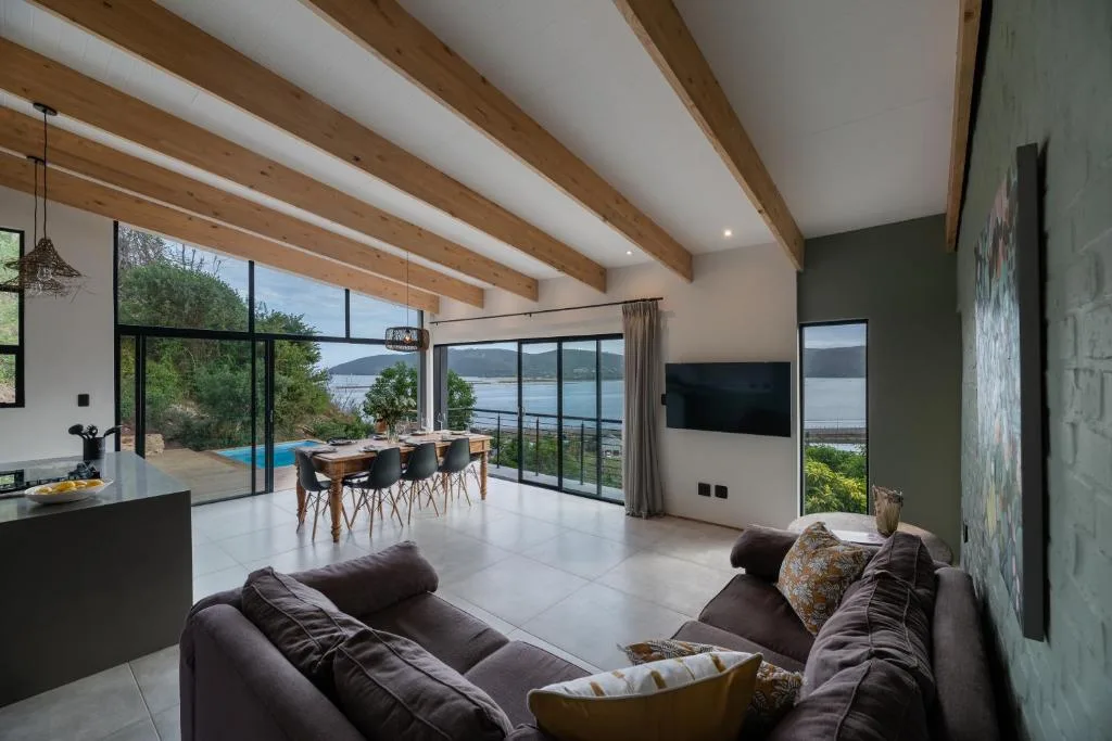 Modern lounge with sofa, dining area, and lagoon views through floor-to-ceiling windows