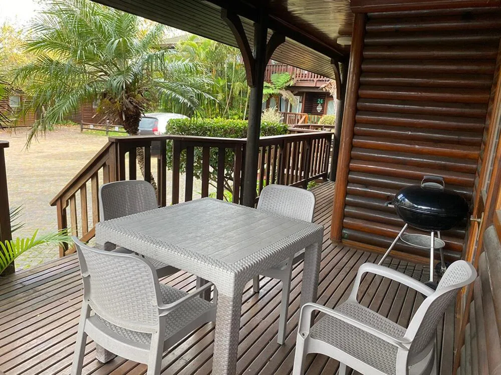 Covered wooden deck with dining table, four chairs, and braai grill